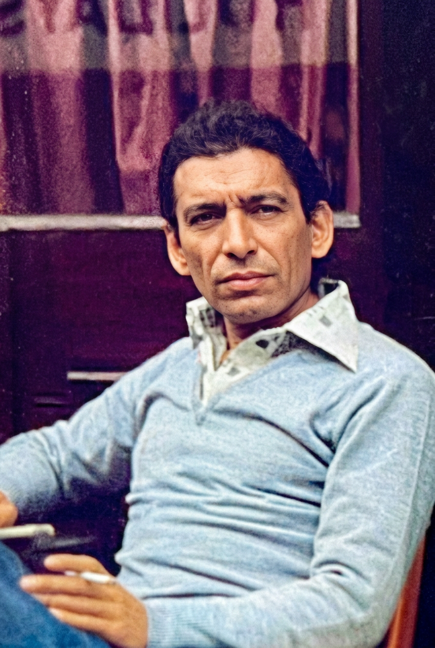 Portrait of Iranian playwright and director Bijan Mofid, wearing a light blue sweater and holding a cigarette, looking directly at the camera.
